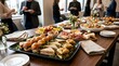 © Noyon - Gourmet assorted mini sandwiches arranged on black platter for professional catering event with people networking in bright office background.