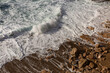 © Simplementbeau. - Bord de mer, gros plan sur une vague qui s’échoue sur le sable et la roche brune, mer agitée et vivante, écume de mer blanche