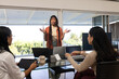 © Wavebreak Media - Diverse female team meeting at glass table, lead in rust cardigan gesturing with laptops tablet