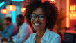 © Viktor - Smiling Black woman with glasses in office with neon lights. Diverse team works behind her. Modern creative workspace with blurred colleagues.