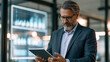 © Yaroslav Stepannikov - Executive reviewing AI generated market insights on tablet, strategic planning, enterprise AI, business innovation, leadership, modern office, premium stock photography