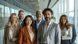 © SolaruS - A diverse group of smiling, confident business professionals stands together in a bright, modern corporate office corridor, embodying successful teamwork, unity, and leadership.
