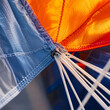 © ARTFUL - Close detail of colorful parachute canopy fabric with orange blue and translucent panels taut suspension lines and stitched seams showing outdoor adventure gear texture and motion ready equipment