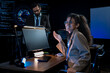 © ultramansk - South Asian male and Black female cybersecurity analysts point at threat monitors discussing solutions in a dark operations center.