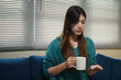 © Prathankarnpap - Young Asian Woman Hesitating to Take Medicine Pills While Holding a Mug at Home