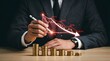 © ShazilStock - Businessman pointing at a failing red financial stock market downward trend line over a wooden desk with shrinking stacks of gold coins against black