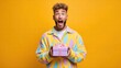 © StockAlchemy - Excited man holding a gift box with a surprised expression against a yellow background.