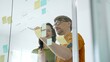 © Hanna - Business colleagues brainstorming innovative ideas during agile meeting, discussing project strategy, developing creative solutions with sticky notes on glass wall in modern office