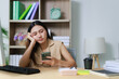 © Tj - Young Asian woman feeling disengaged during her workday, using her mobile phone instead of focusing on tasks, showing signs of weariness and lack of motivation