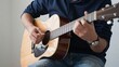 © Studicon - Close up of a person playing an acoustic guitar while wearing a navy polo and blue jeans
