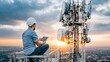 © Ben - Telecommunication engineer inspecting cell tower equipment using digital tablet while sitting on railing at sunset with city view