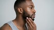 © Yassine - Handsome young african american man touching his well groomed beard while looking away against a clean light grey studio background