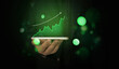 © visuals6x - Businessman holding smartphone with glowing green financial growth chart hologram above screen.
