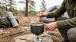© Xenia - Person stirring food in a camping pot on a portable gas stove. Outdoor cooking during a hiking trip in the forest
