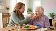 © Megin Design - Female caregiver feeding a senior woman in a wheelchair. Elderly care assistance during a healthy meal with salmon and vegetables