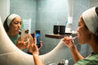 © Marko Geber - Young woman brushing teeth while recording a mirror selfie in home bathroom