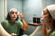 © Marko Geber - Woman applying facial mask in bathroom mirror
