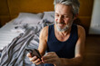 © Davor - Smiling middle-aged man using smartphone in home bedroom