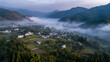 © 琛明 周 - Misty Morning Village in Mountains: A picturesque village nestled amidst rolling mountains is enveloped in a soft blanket of morning mist, creating a serene and tranquil atmosphere.