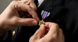 © TRI WAHYUNI - Close up of hands pinning a golden military medal on a dark suit jacket