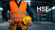 © MdAbul - Worker holding hard hat with HSE health safety environment concept text
