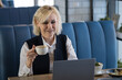 © lenblr - Woman Drinking Coffee. Professional Elderly Woman Seated Comfortably With Beverage During Midday Pause. Casual Businesswoman In White Attire Savoring Her Morning Coffee In Cozy Setting