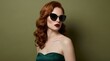 © Yassine - Elegant woman with long wavy red hair posing in dark sunglasses while wearing a glamorous green satin strapless evening dress