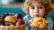 © Aliaksandra - Curly-haired child holds French fries beside a basket containing a cheeseburger and fresh fruit, illustrating childhood nutrition and food choice