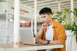© bongkarn - Asian man focused on browsing online with laptop while sitting at table in a contemporary cafe.