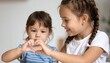© Assets Management - Two young girls making a Korean finger heart gesture together indoors