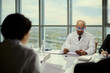 © DragonImages - Medium shot of middle aged male doctor reviewing paperwork during meeting with colleagues, discussing medical administration and leadership. Ideal for healthcare management or policy marketing