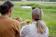 © Ina - Middle aged couple enjoying picnic meal while looking across open countryside landscape. Shared outdoor dining experience, family bonding and relaxed weekend recreation concept.