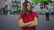 © Krakenimages.com - Young hispanic woman with arms crossed on a city street, grimacing in a red tshirt; frustration rejection.