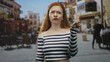 © Krakenimages.com - Redhead woman pointing finger with hand on hip in a street cafe scene with outdoor tables and an umbrella visible; annoyance.