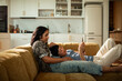 © Marko Geber - Two women relaxing on sofa with smartphone in modern home kitchen