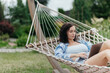© Валерия Стоганенко - Beautiful woman resting comfortably in a hammock after remote work with a laptop nearby. Digital nomad lifestyle, work-life balance