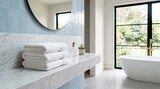 Bright Modern Luxury Bathroom With Marble Vanity, Folded Towels, Round Mirror, Freestanding Bathtub And Natural Window View