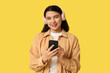 © Pixel-Shot - Pretty young woman with mobile phone and headphones listening to audiobook on yellow background