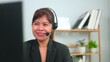 © Thawatchai Images - Professional Asian female customer service operator wearing a headset working on a computer, talking happily with clients in a friendly remote workspace office environment.