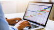 © Sabbir Media - Business person typing on laptop with a colorful gantt chart for project management and planning