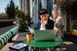 © Davor - Focused businesswoman reviewing documents on laptop at outdoor cafe