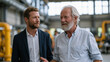 © forenna - Business succession planning consultant walking side by side with a retiring factory owner through the production floor, the older man gesturing toward equipment and employees he