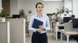 © Sofia - Professional female assistant holding blue folder in office. Confident businesswoman standing in modern workspace. Corporate career and organization concept