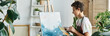 © LIGHTFIELD STUDIOS - A young woman enjoys her artistic hobby, painting a vibrant piece in her welcoming home filled with plants, banner