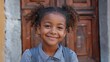 © Harry - Delightful young girl with curly hair smiles brightly against rustic wooden door and stone wall in soft focus.
