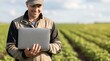 © Eve - Happy professional farmer agronomist in uniform cap standing in agricultural field using laptop computer. Concept of modern smart farming technology and agricultural business. High quality stock