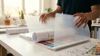 © Photo Moon - Architecture Design - Designer Lifting Transparent Tracing Paper Over Blueprint Rolls and Color Swatches on White Desk