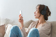 © buritora - A relaxed woman sitting on a sofa at home, listening to music with headphones on.