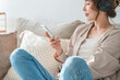 © buritora - A relaxed woman sitting on a sofa at home, listening to music with headphones on.