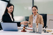 © NINENII - Two Asian women lawyers review real estate contracts with a model house, property law, investment, legal advice, and consultation concepts.